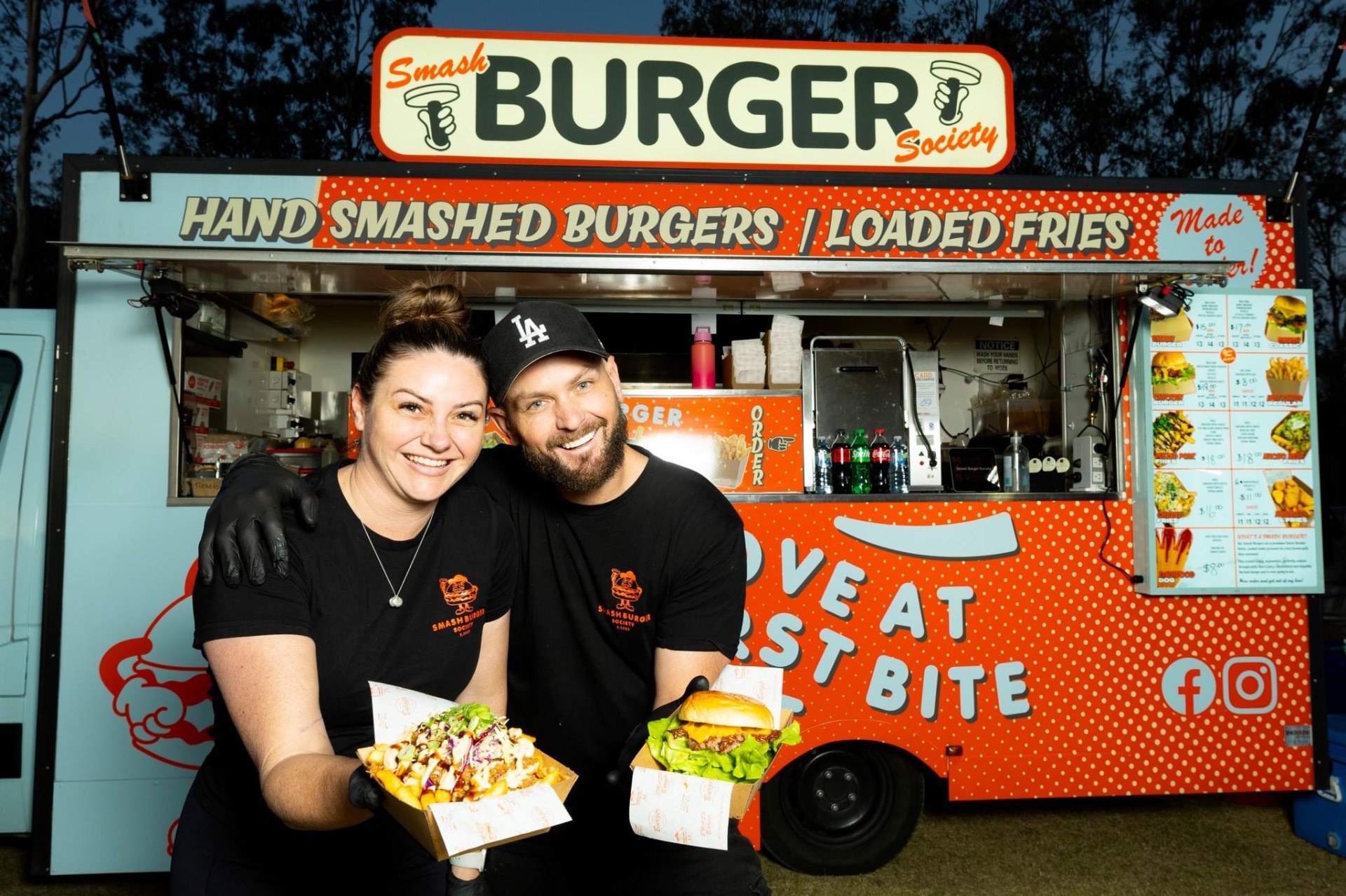The Smash Burger Society owners standing in front of their food truck with burgers and loaded fries